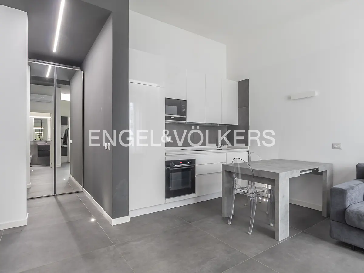 Modern kitchen with white cabinets, stainless steel appliances, a grey dining table, and transparent chairs on tiled floors.