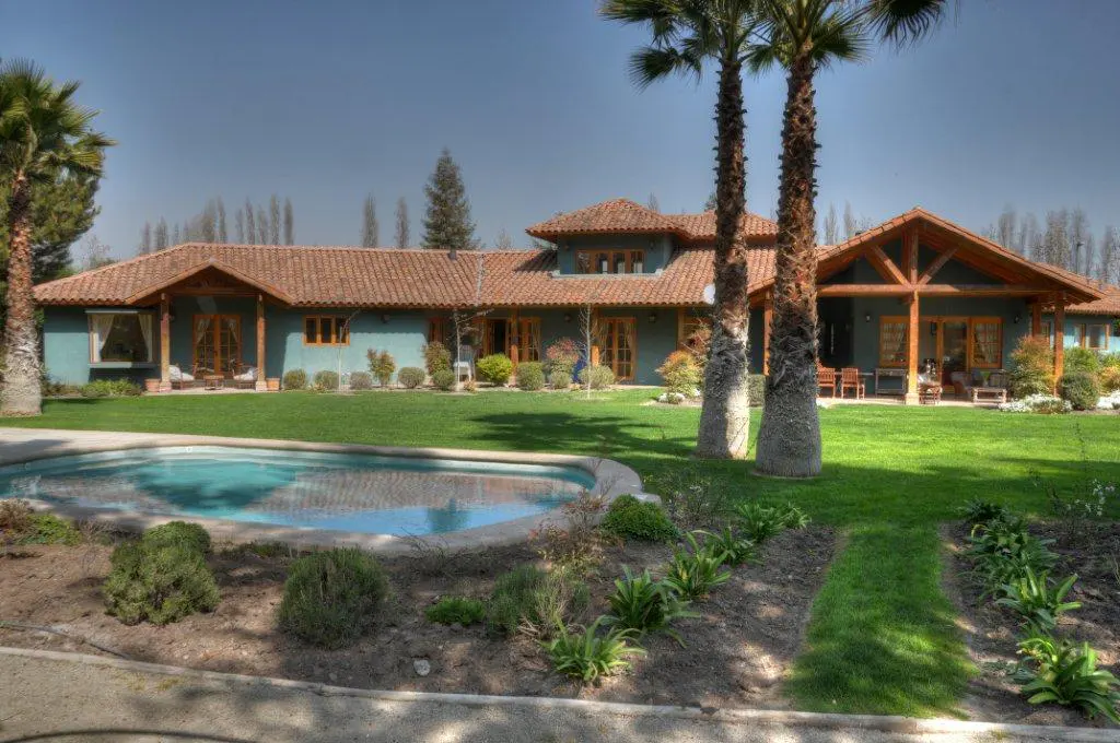 Exterior of a teal house with a red tile roof, palm trees, and a kidney-shaped pool.