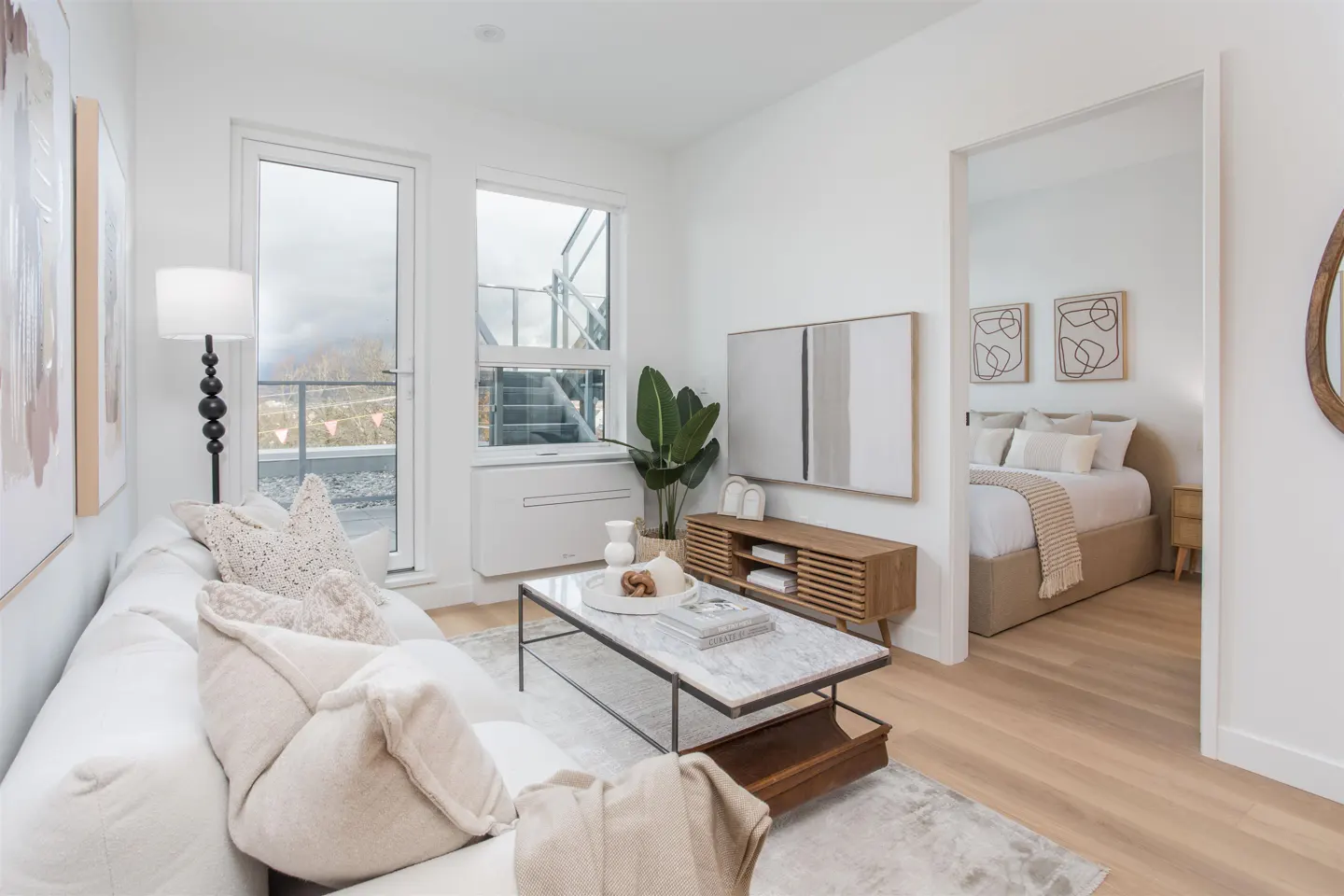 Bright, modern living room with white sofa, marble coffee table, and wood media console. Bedroom visible through doorway. Balcony access.