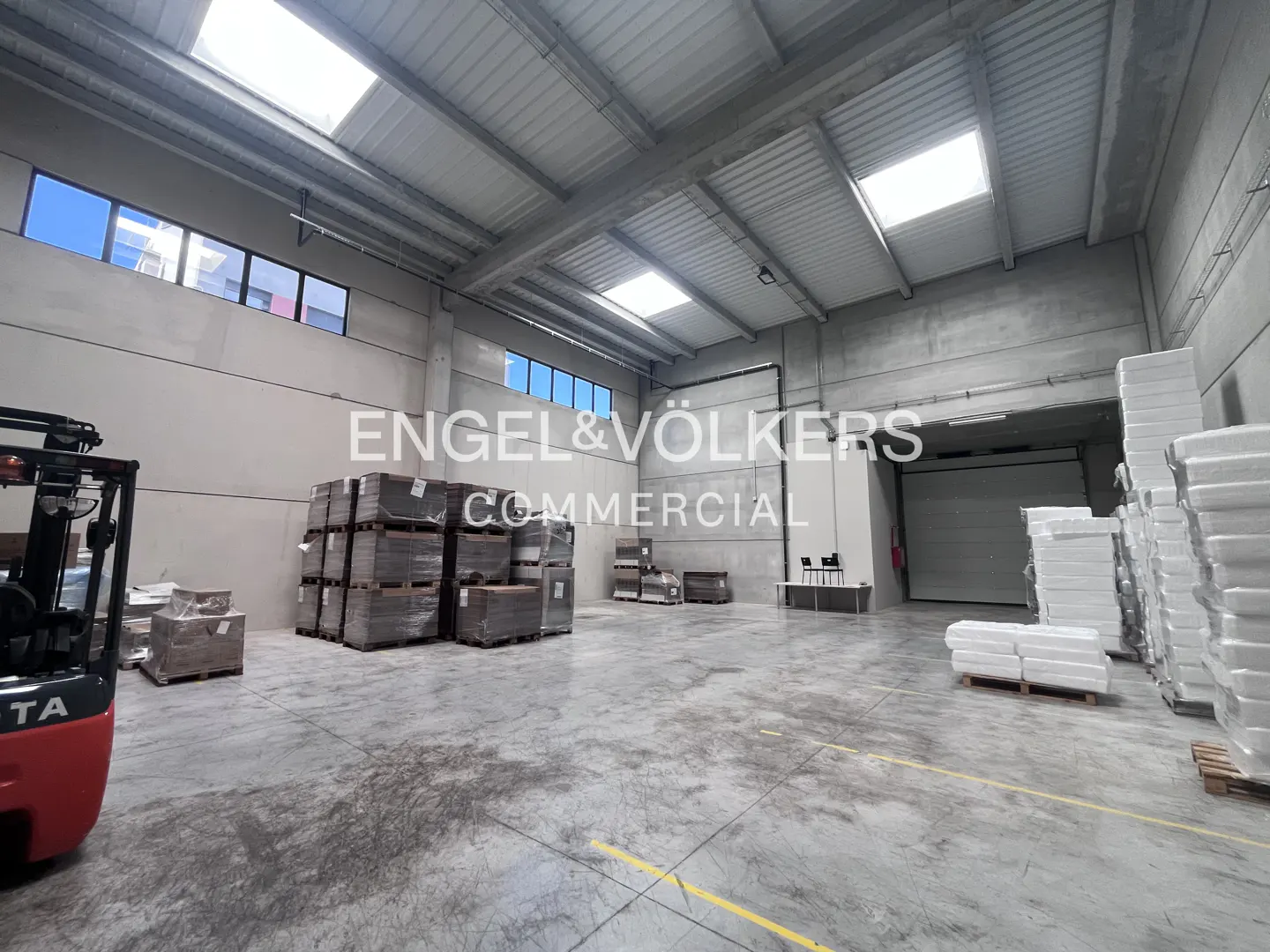 A large, empty warehouse with a forklift, pallets, and the Engel & Völkers logo.
