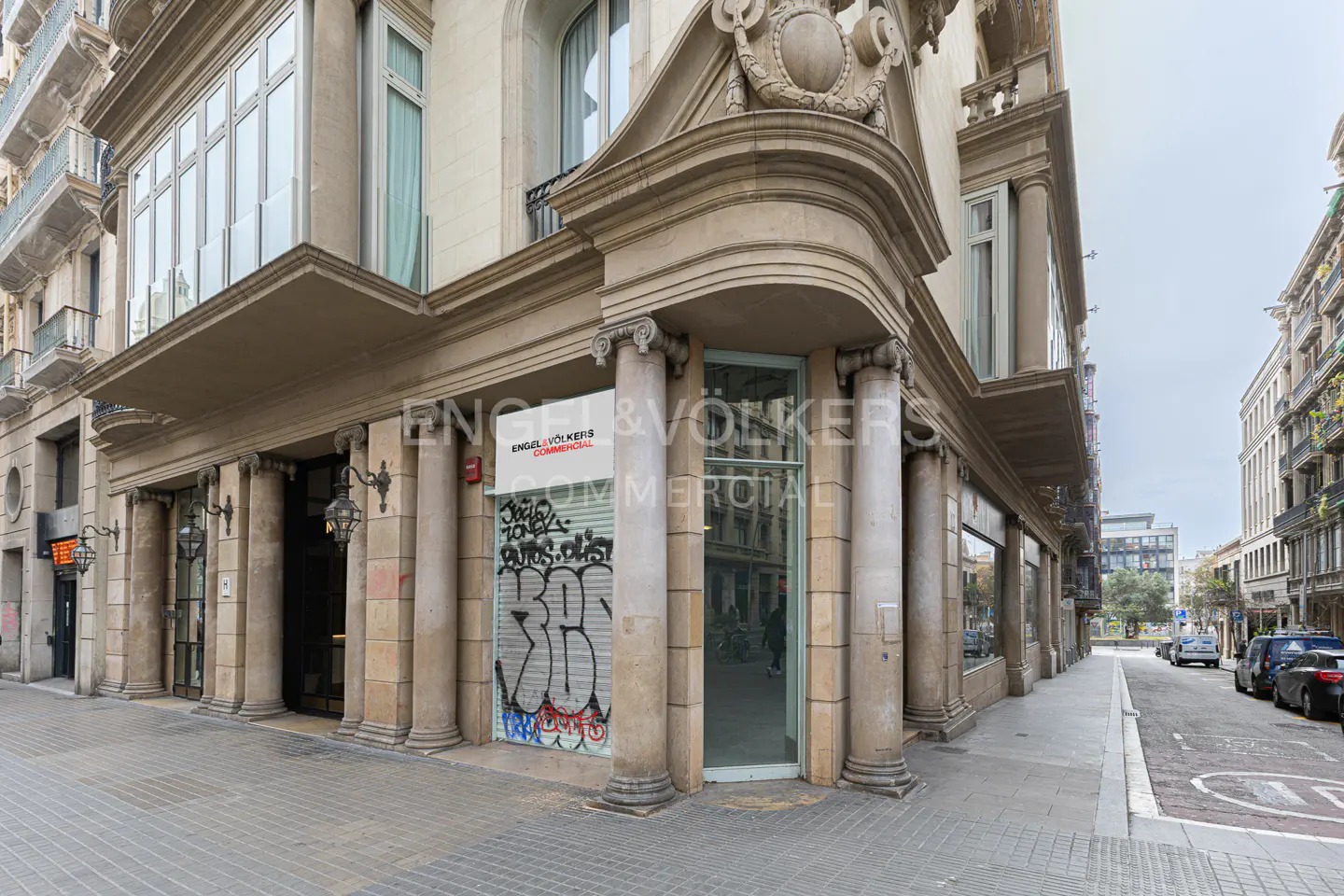 Exterior view of a commercial building with an Engel & Völkers sign. The building has columns and graffiti on the closed storefront.