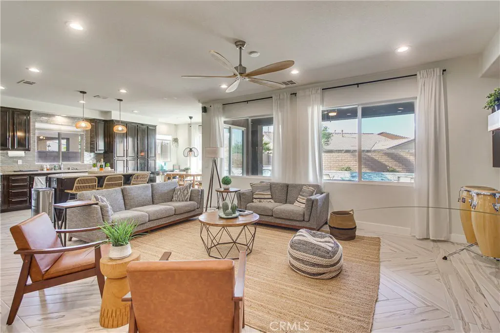 Open-concept living room with gray sofas, brown leather chairs, and a jute rug. Kitchen with dark cabinets in the background.