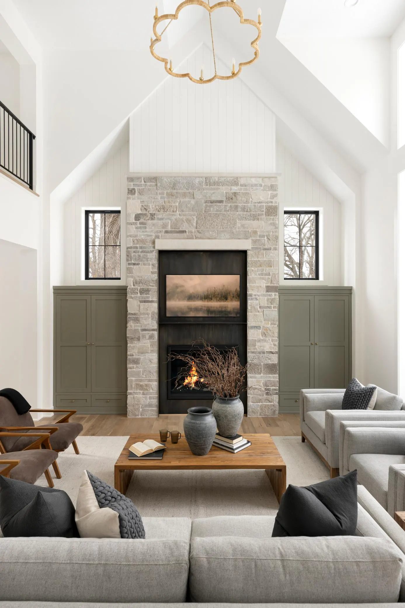 Bright living room with vaulted ceiling, stone fireplace, and gray sofas. A wooden coffee table sits in the center.