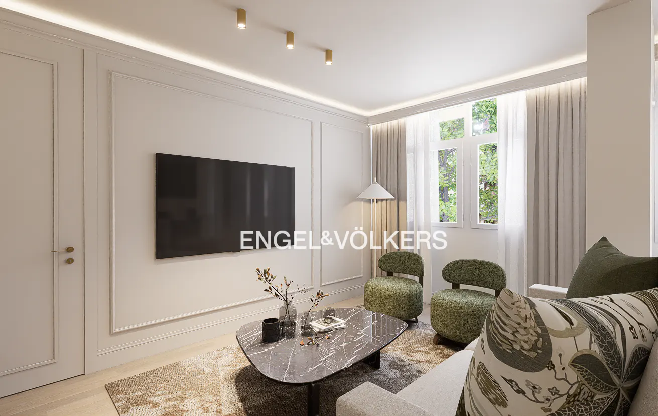 Modern living room with a wall-mounted TV, two green armchairs, a marble coffee table, and a patterned sofa.