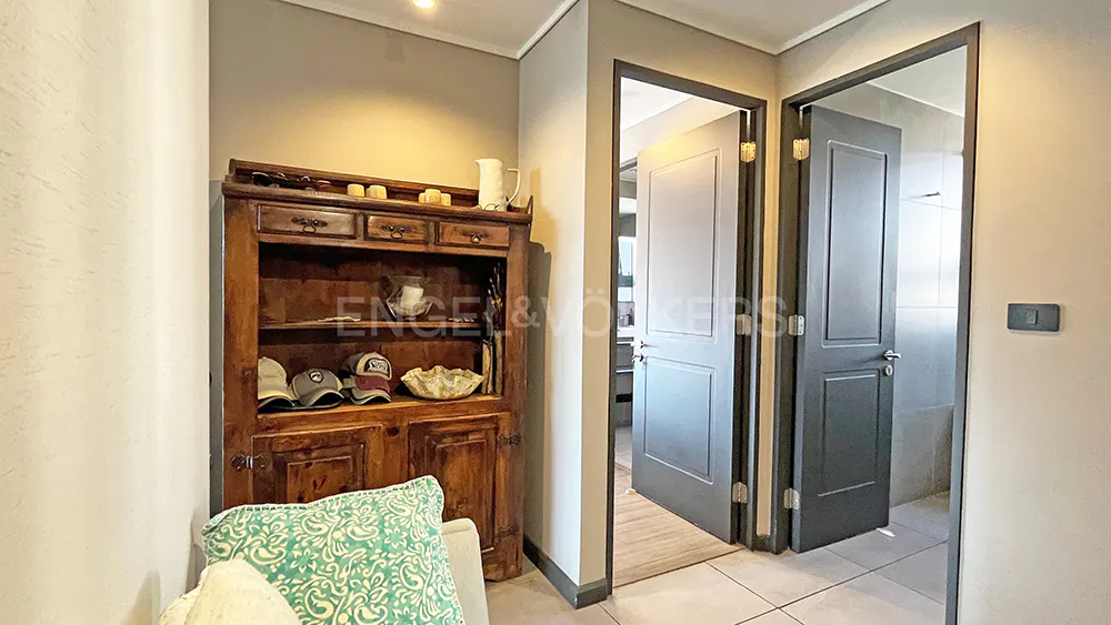 A hallway with a wooden cabinet, hats, and decorative items. Two open doors lead to other rooms. The walls are light beige.