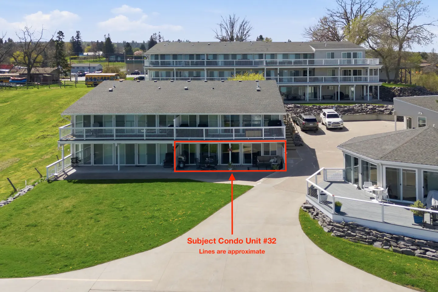 Condo building with gray roof and white siding. Unit #32 is outlined in red, with a patio and sliding glass doors. Green lawn in the foreground.