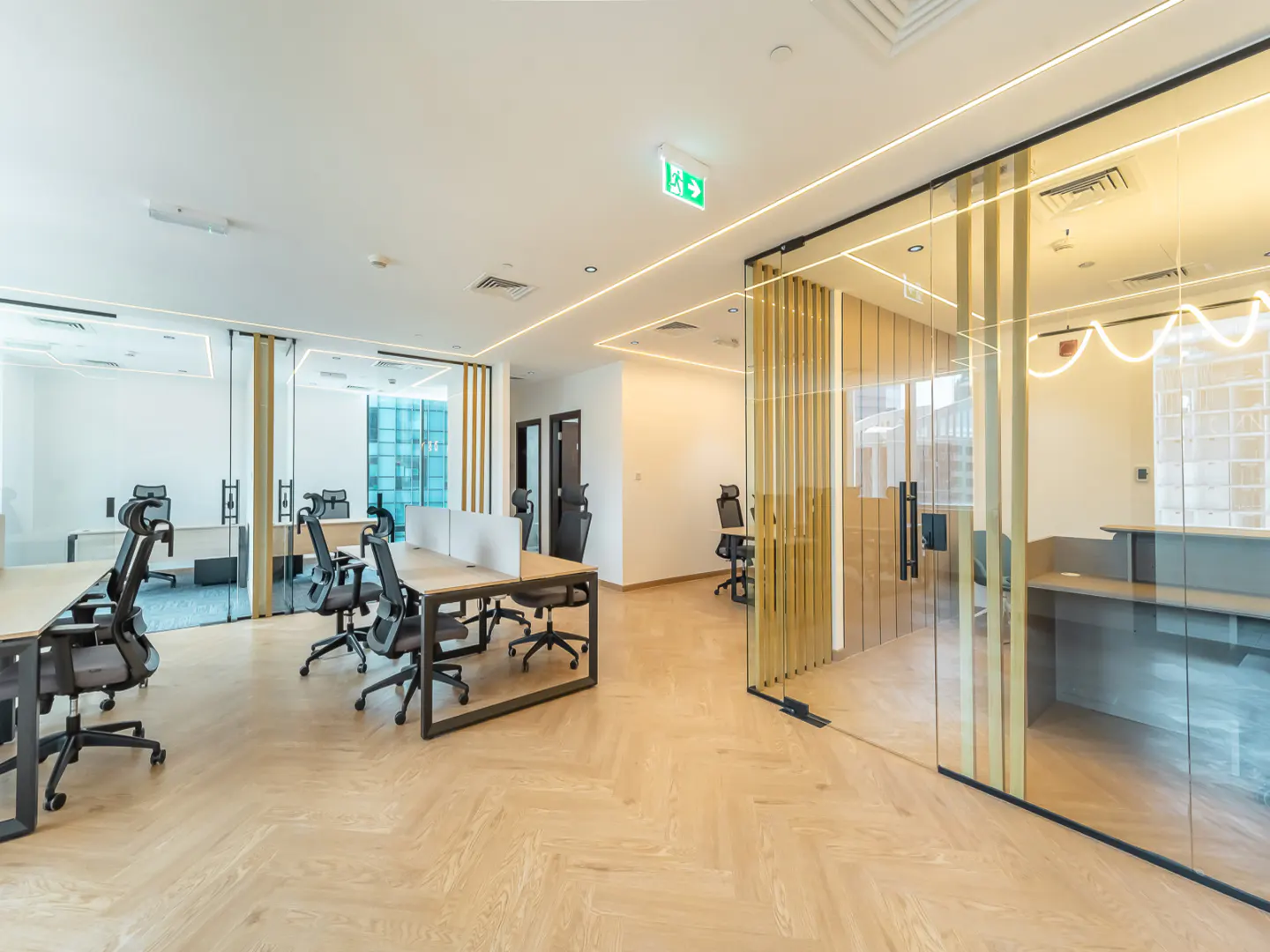 Bright, modern office space with wood floors, glass-walled offices, and black office chairs around light wood desks.