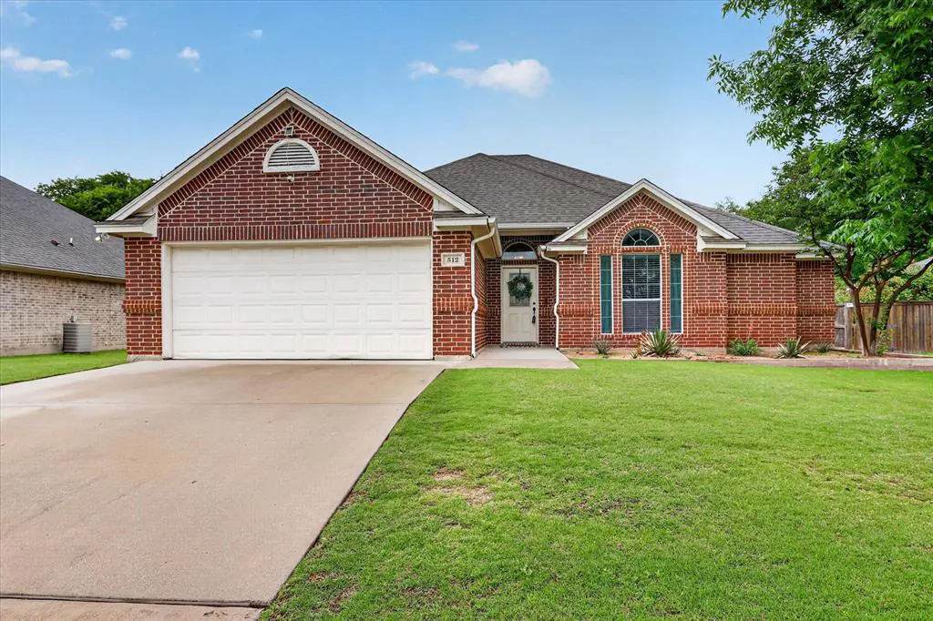 Red brick, one-story house with a white garage door and a green lawn under a blue sky.