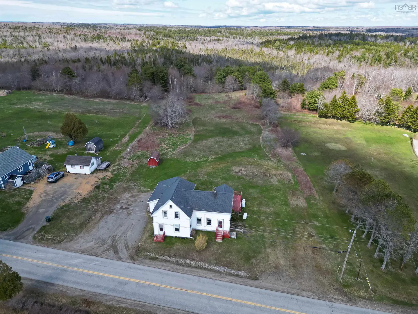 Aerial view of a white two-story house with a gray roof, red porch, and green lawn, with a forest in the background.