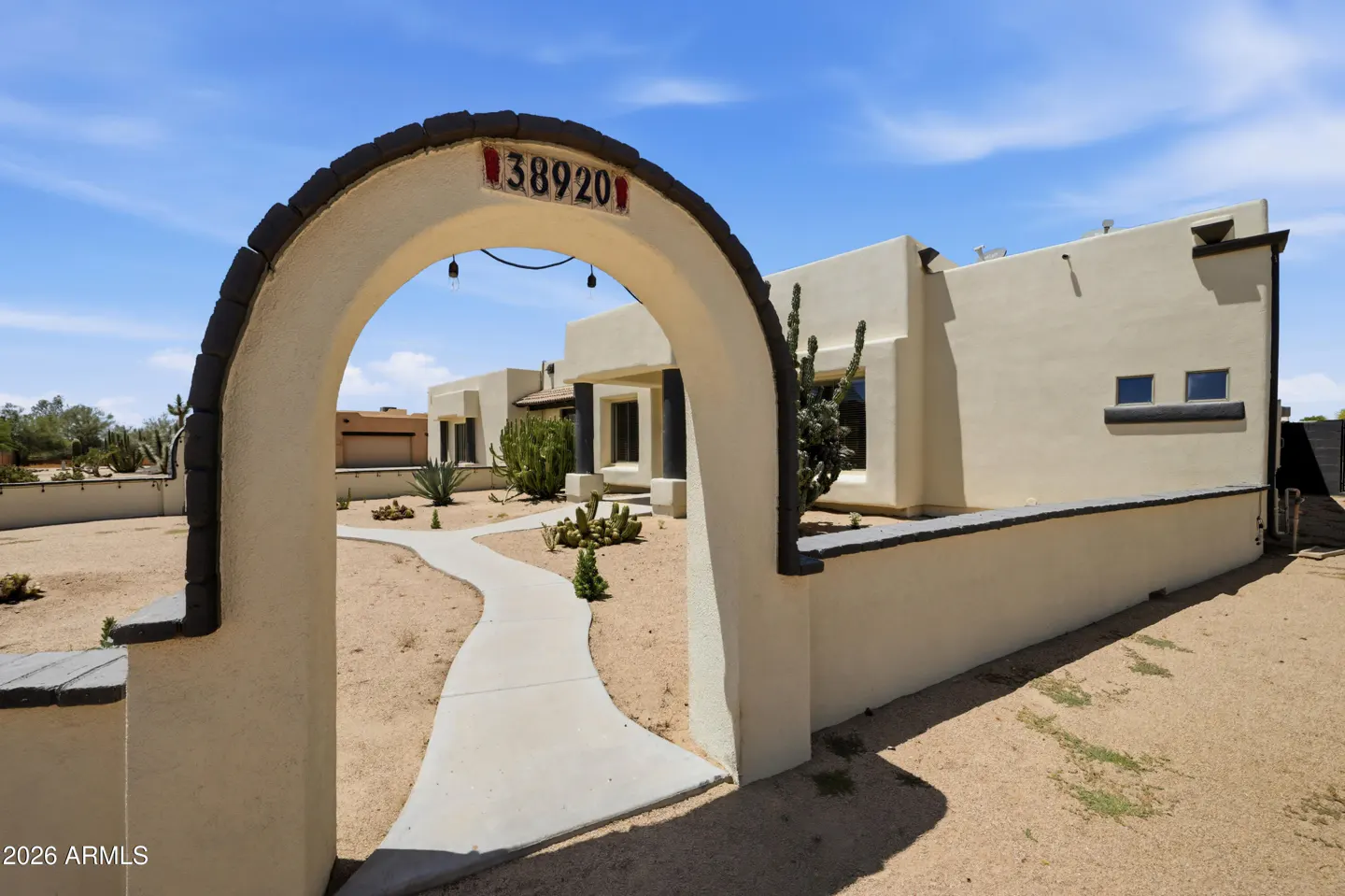 A tan stucco home with a desert landscape, viewed through a decorative arched entryway featuring the address 38920.