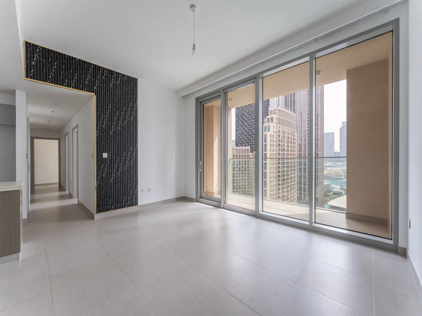 Modern living room with white tile floors, a black marble accent wall, and floor-to-ceiling windows overlooking city towers.