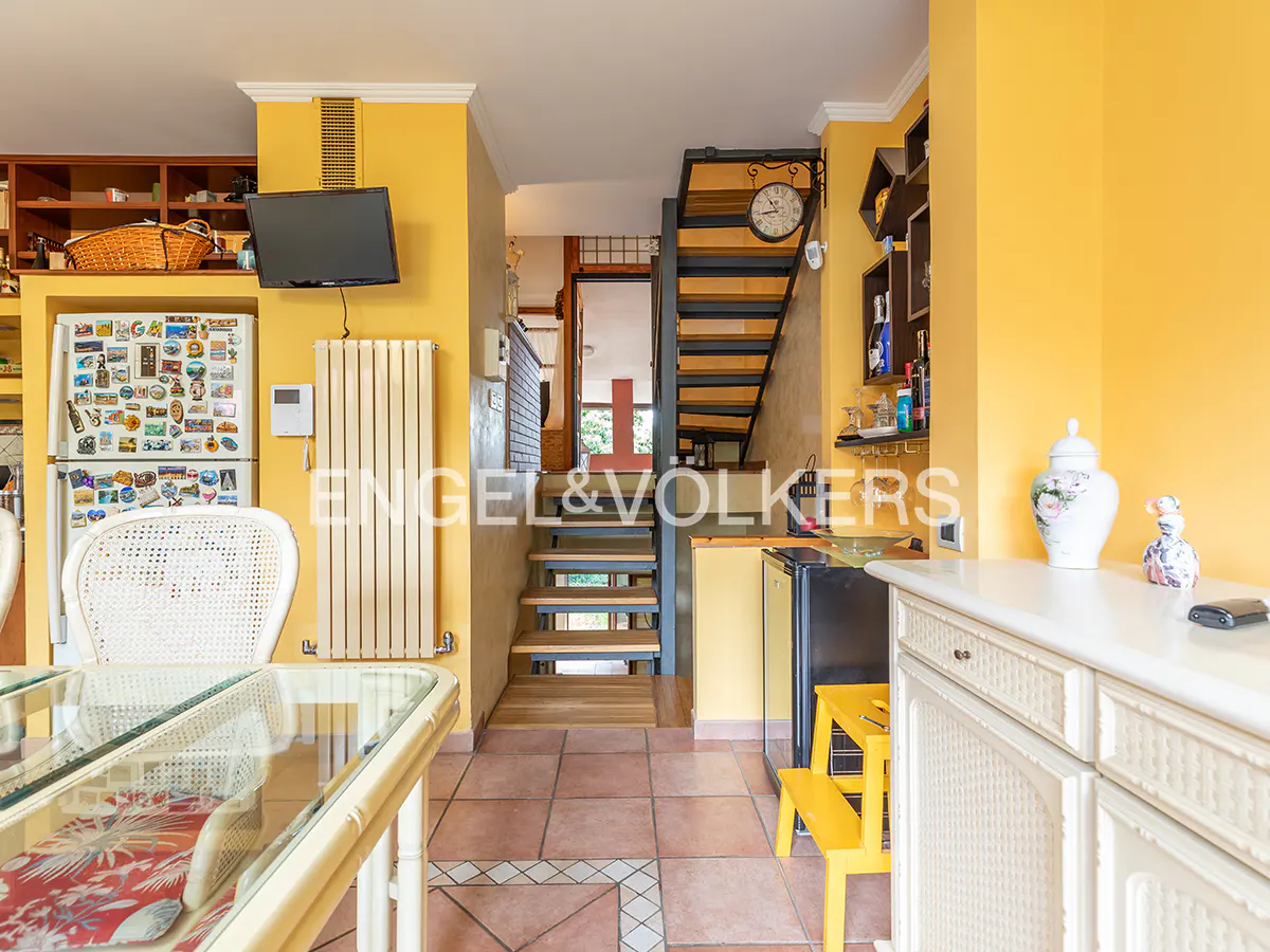 Bright yellow dining area with a glass table, a refrigerator covered in magnets, and stairs leading to an upper level.