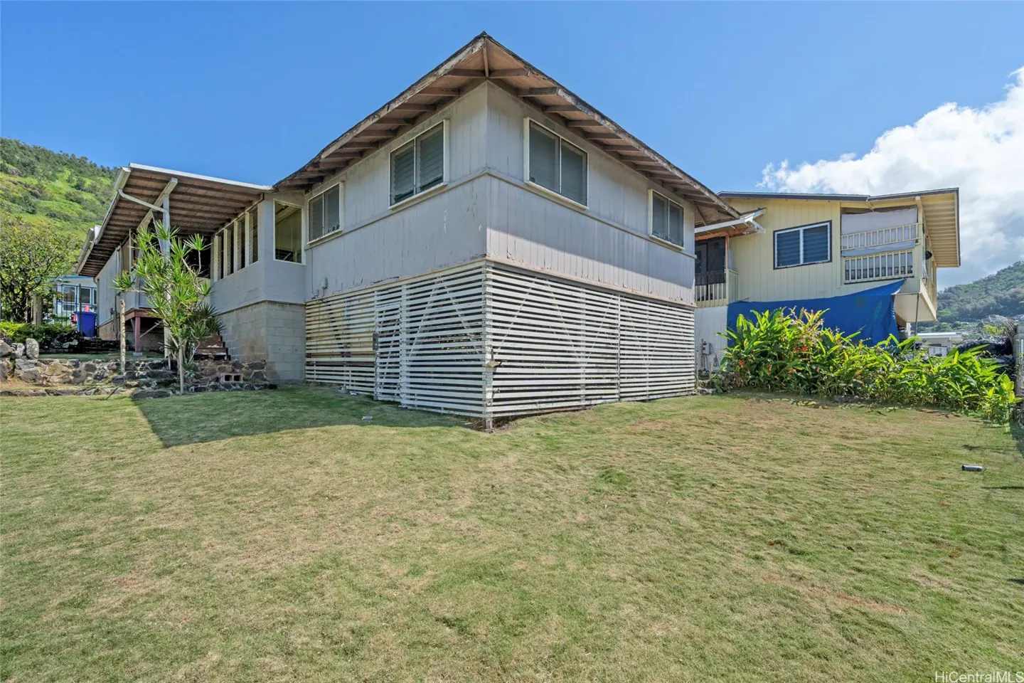 Exterior view of a two-story, light gray house with white lattice skirting and a green lawn under a blue sky.