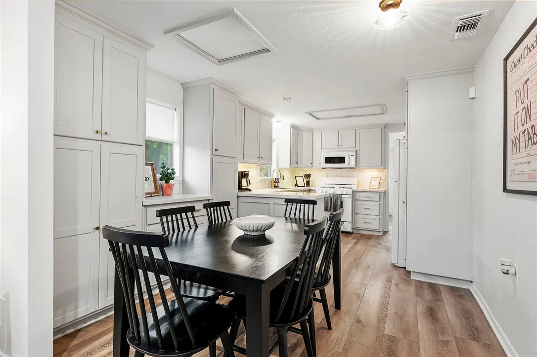 Bright, open kitchen with gray cabinets, wood floors, and a black dining table with six chairs. A white bowl sits in the center of the table.