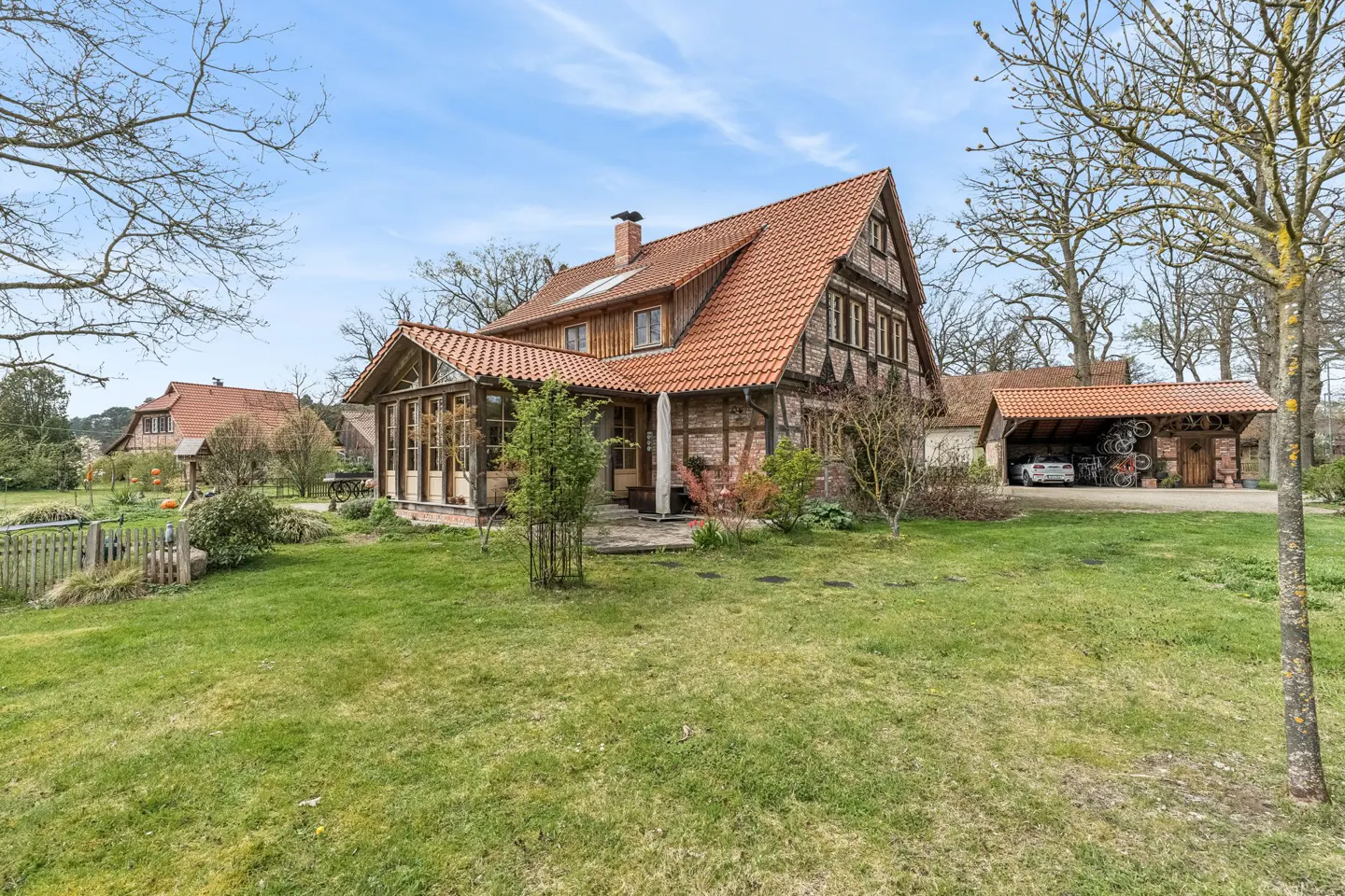Exterior view of a half-timbered house with a red tile roof and a green lawn in front of it on a sunny day.