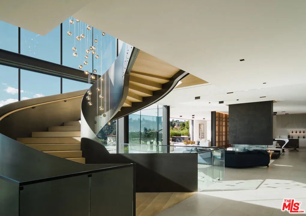 Interior view of a modern home featuring a curved staircase with a chandelier and a spacious living area.