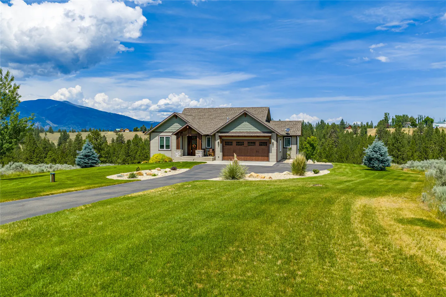 A single-family home with a green lawn, a driveway, and a mountain in the background.