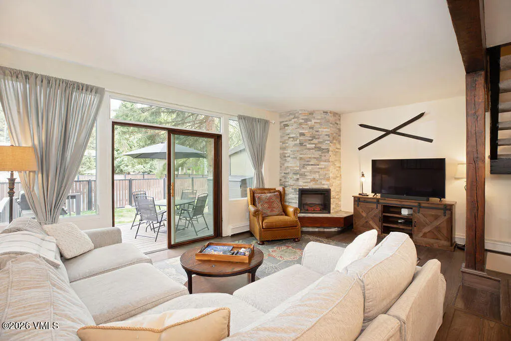 Living room with a stone fireplace, TV, and a sliding glass door to a patio with outdoor seating.