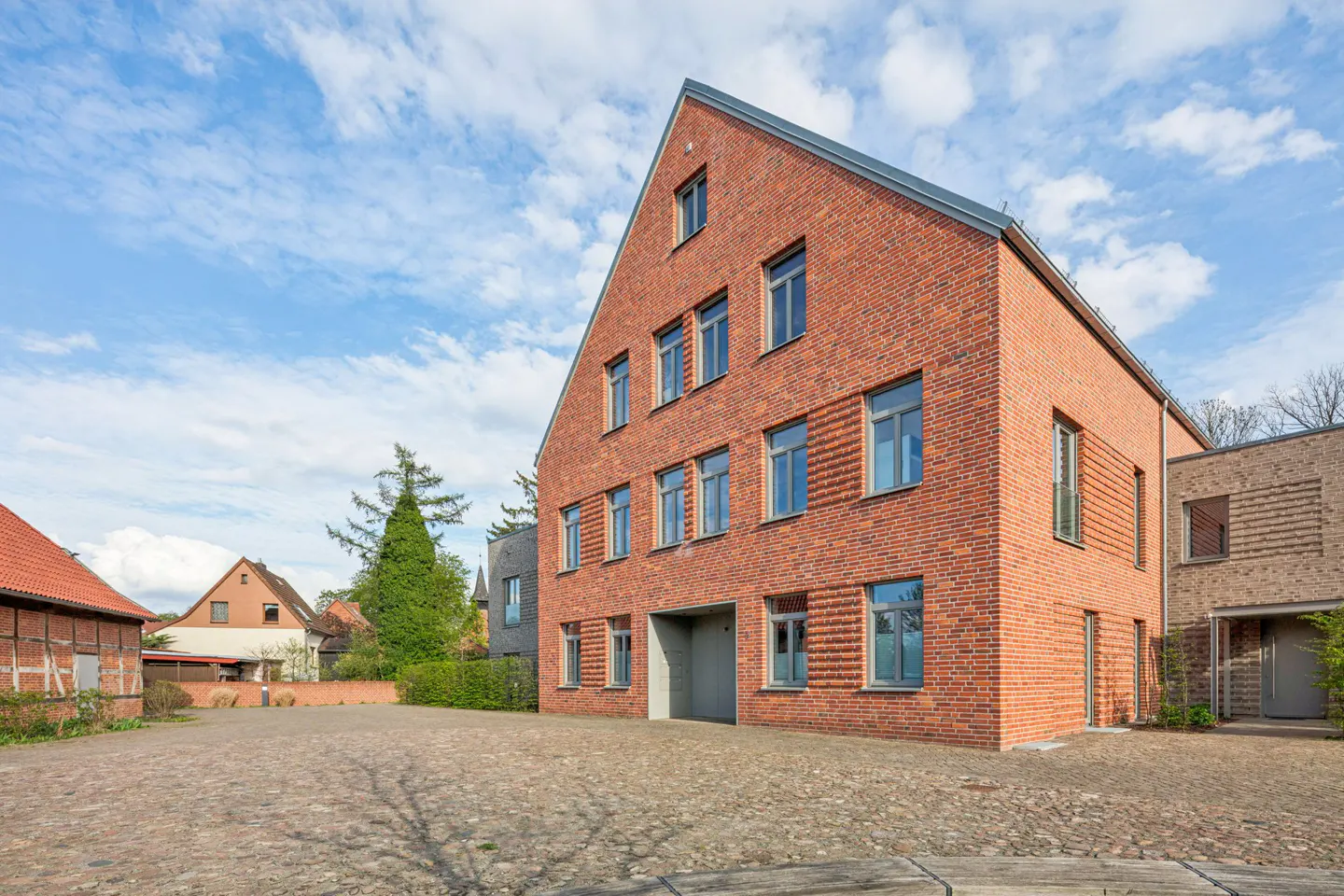 A three-story red brick building with gray trim and a cobblestone courtyard on a sunny day.