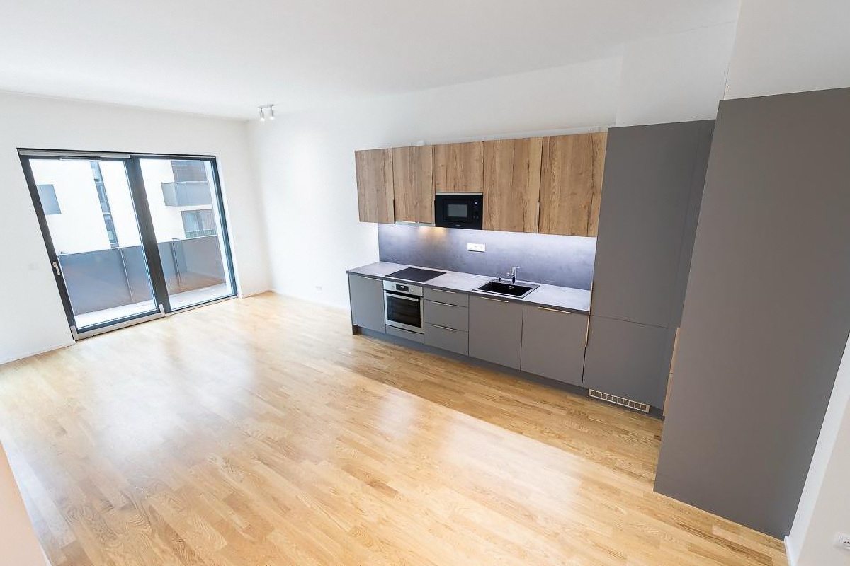 Bright, modern apartment with wood floors, gray cabinets, wood-look upper cabinets, and a sliding glass door to a balcony.