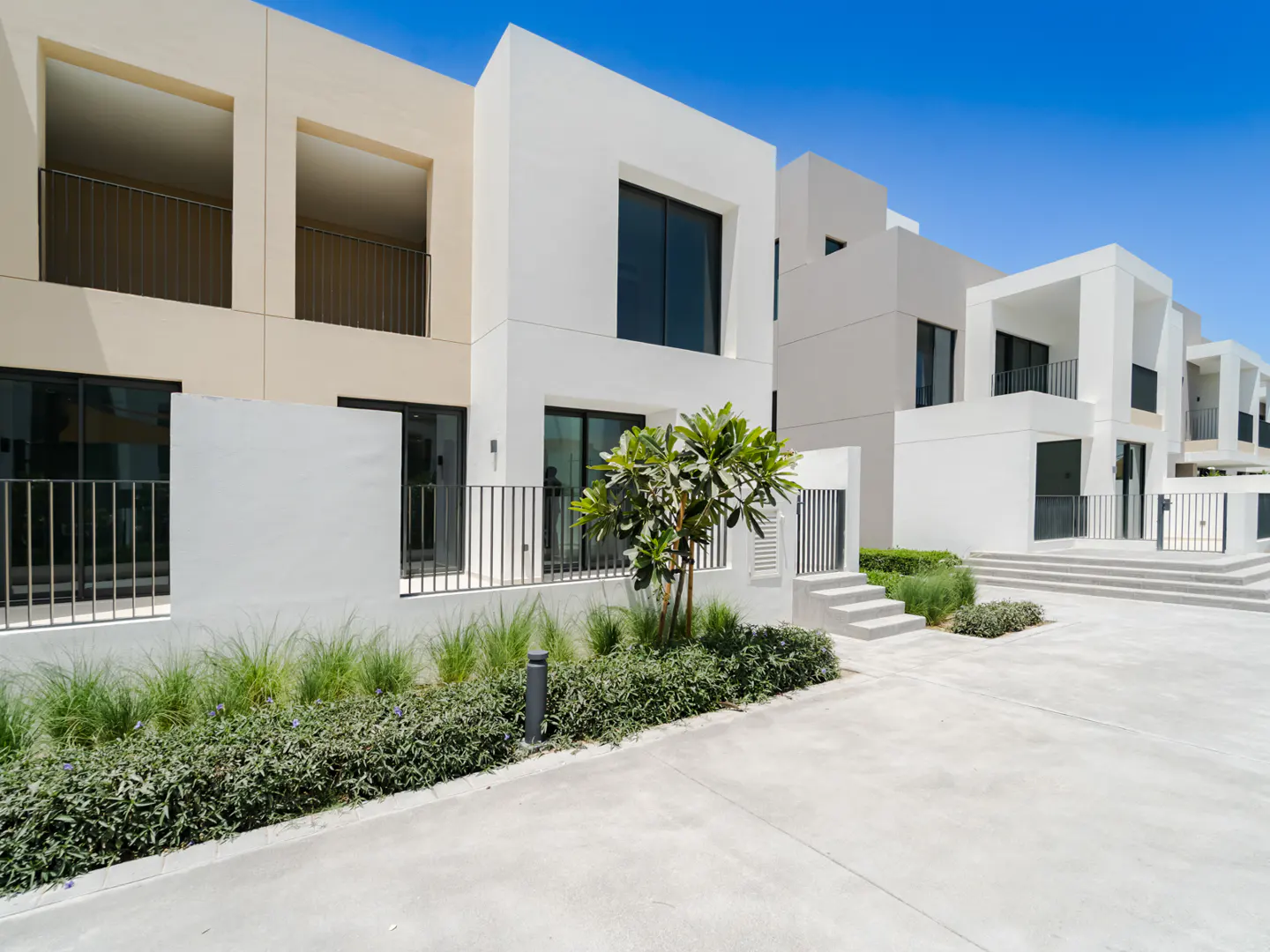 Modern white townhouses with black framed windows and balconies. Green landscaping and a clear blue sky complete the scene.