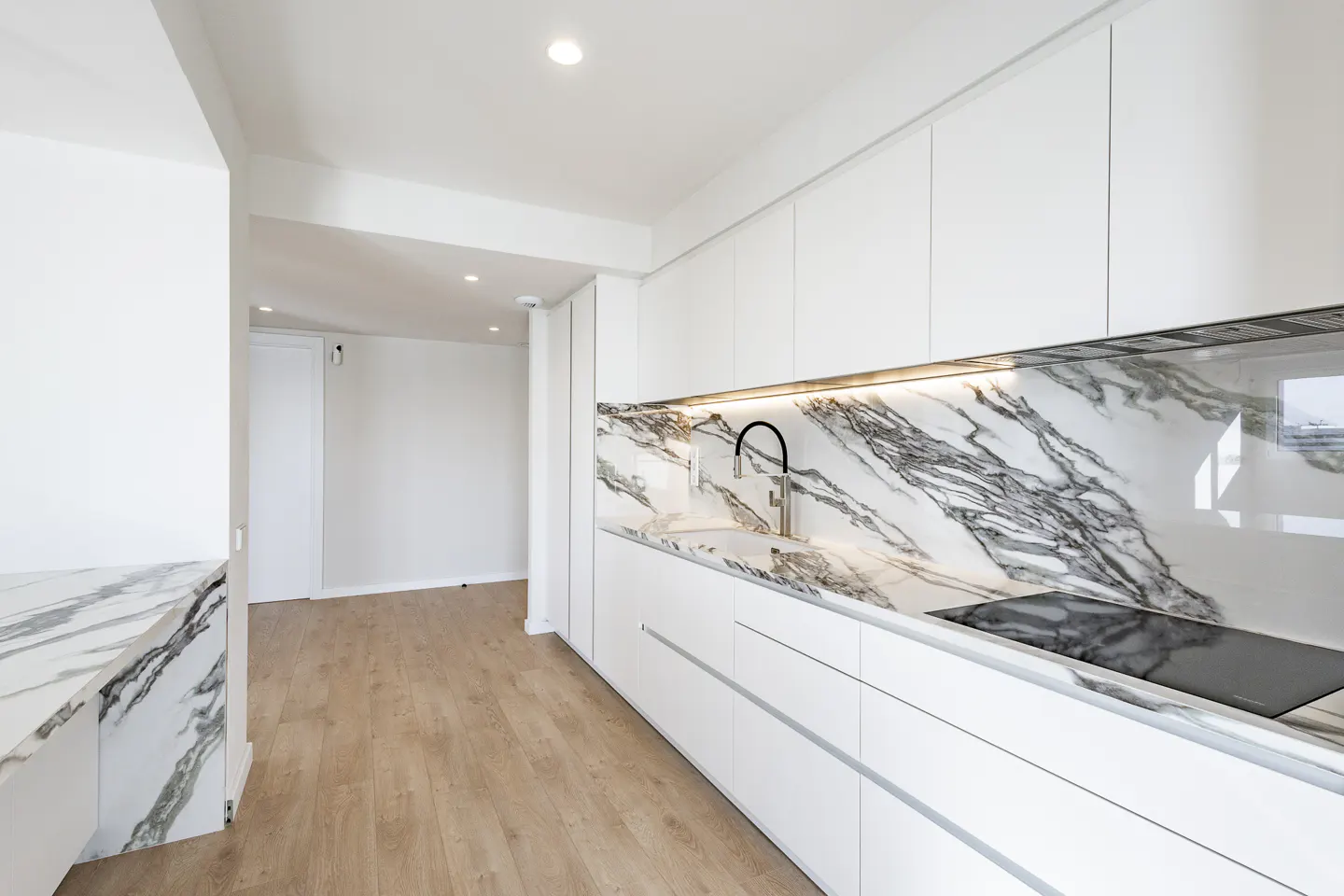 Bright kitchen with white cabinets, marble countertops and backsplash, black faucet, and light wood floors.