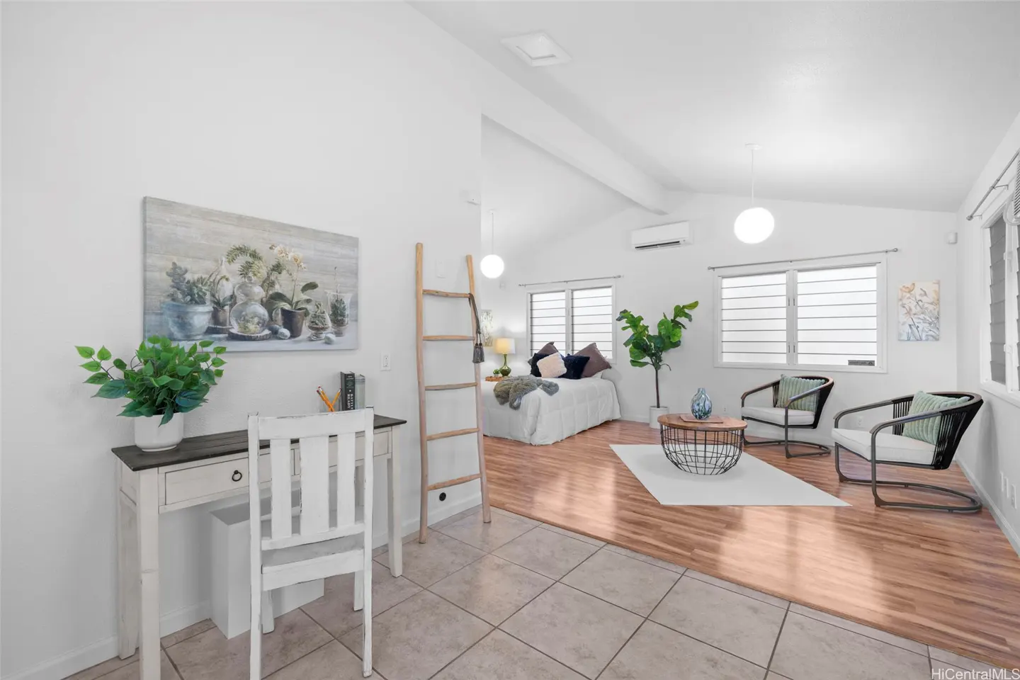 Bright, open-concept living space with a desk, ladder, bed, and seating area. White walls and light wood floors create a clean, modern look.