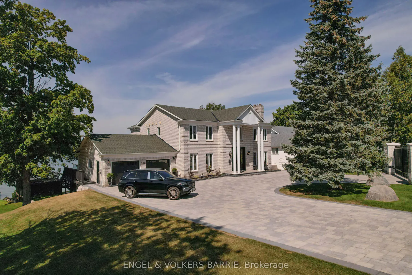 Exterior view of a large, two-story, light-brick house with white columns, a green roof, and a black car parked in the driveway.