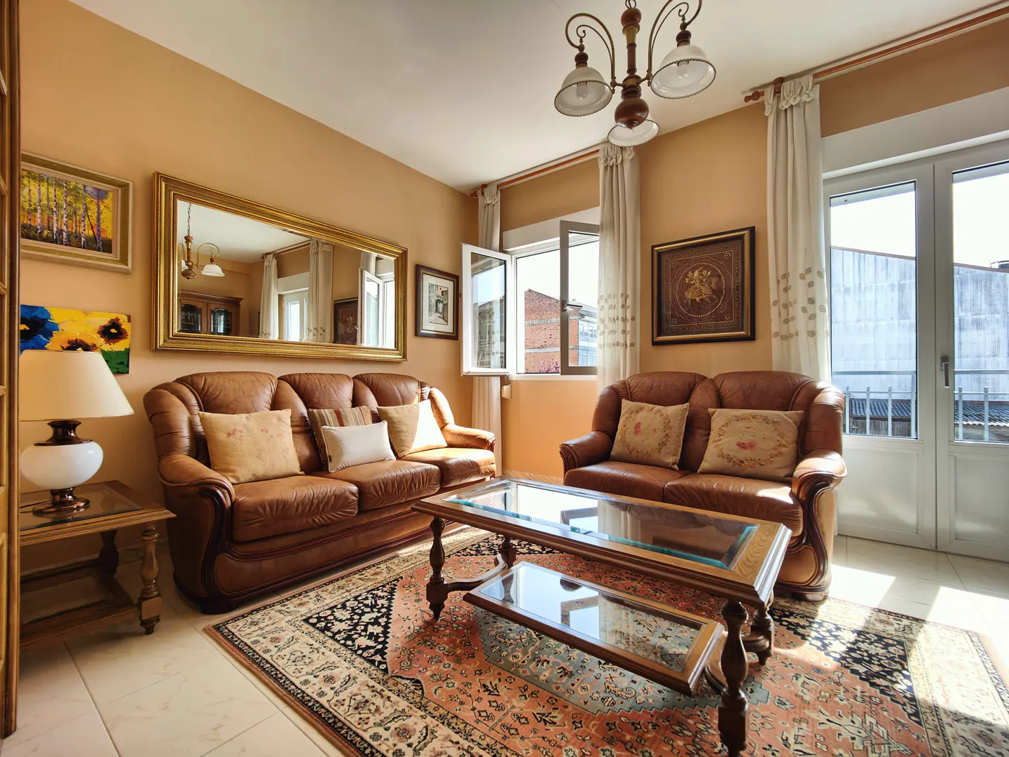 Living room with brown leather sofas, glass coffee table, and patterned rug. Art adorns the peach walls, and natural light streams through the window.