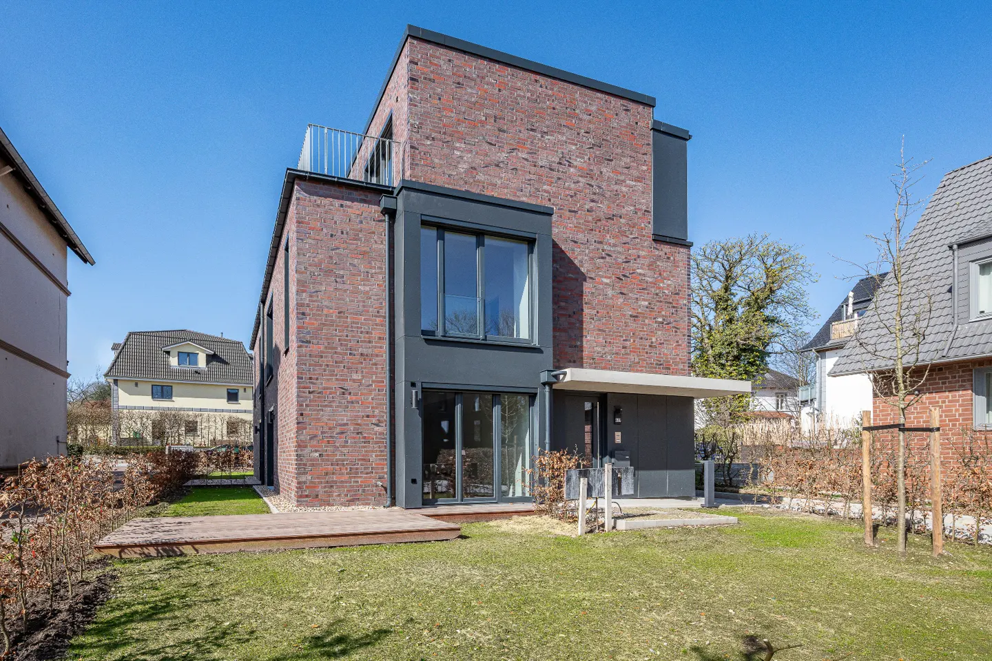 Modern brick house with black trim, a small balcony, and a green lawn on a sunny day.