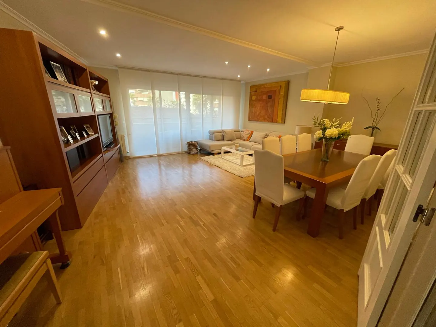 Spacious living and dining room with hardwood floors, a large wooden bookshelf, dining table, and sectional sofa.