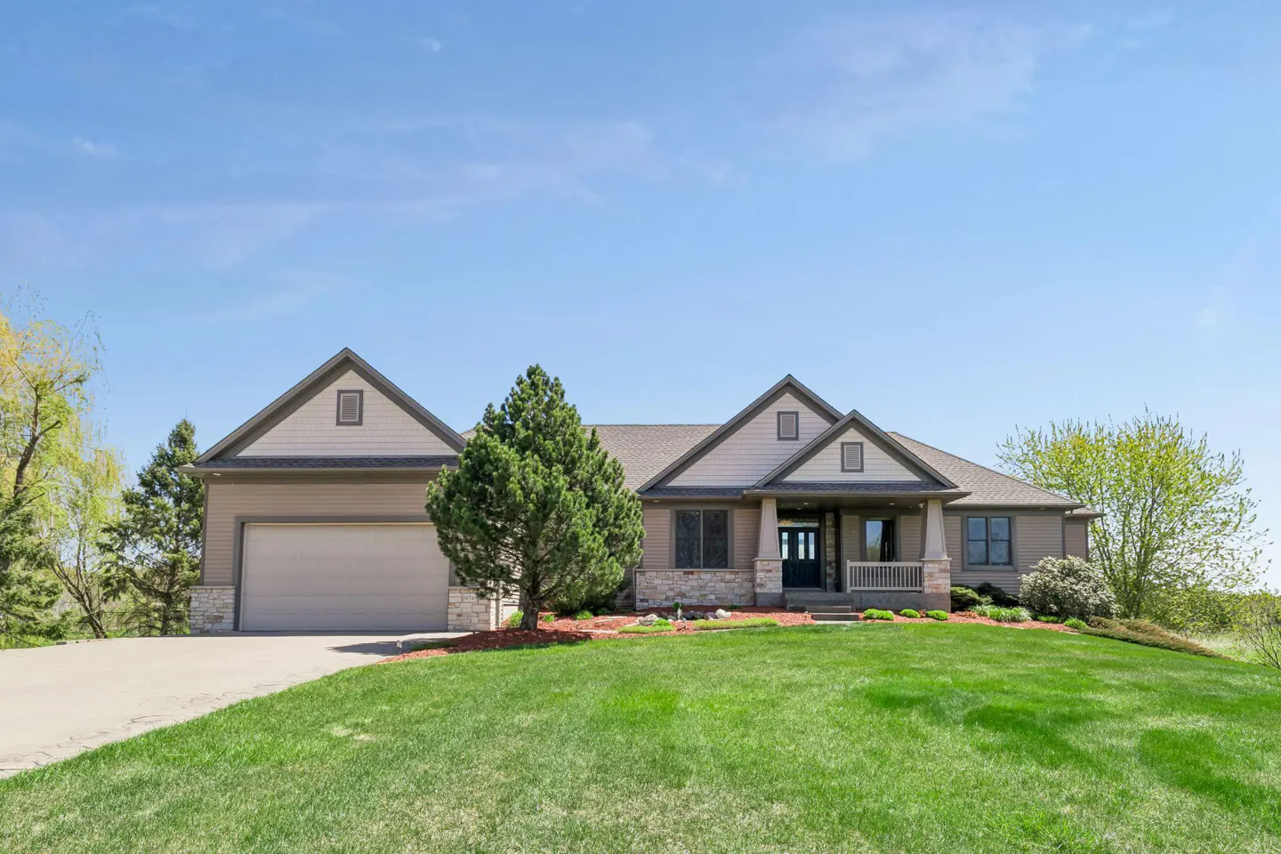 A tan single-story house with a gray roof, a two-car garage, and a green lawn under a blue sky.