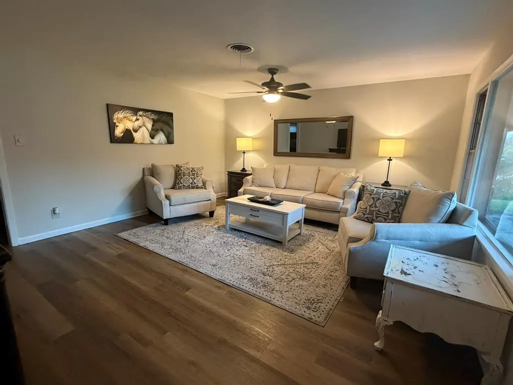 Living room with beige sofa, two armchairs, and a white coffee table on a patterned rug. A horse painting hangs on the wall.
