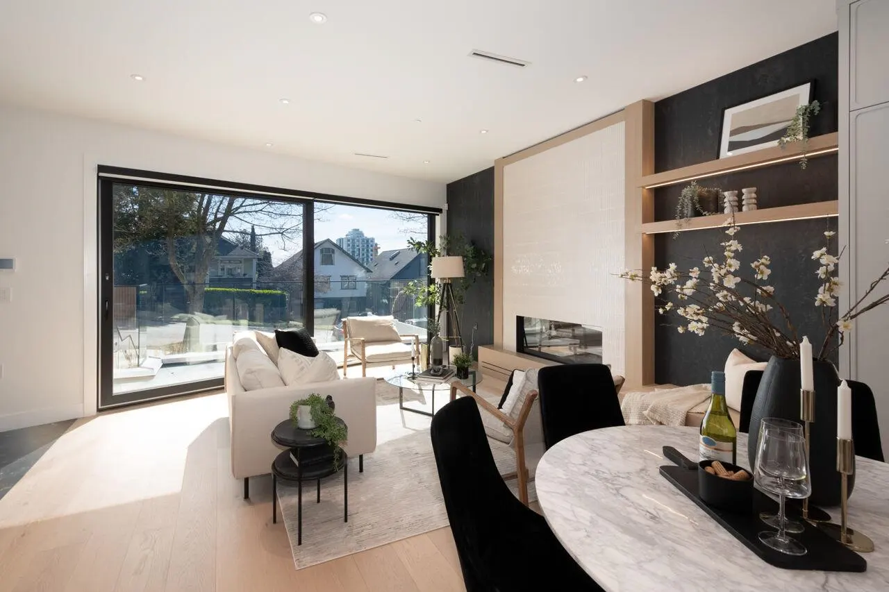 Bright, modern living room with a white sofa, marble table, and large windows overlooking a residential street.