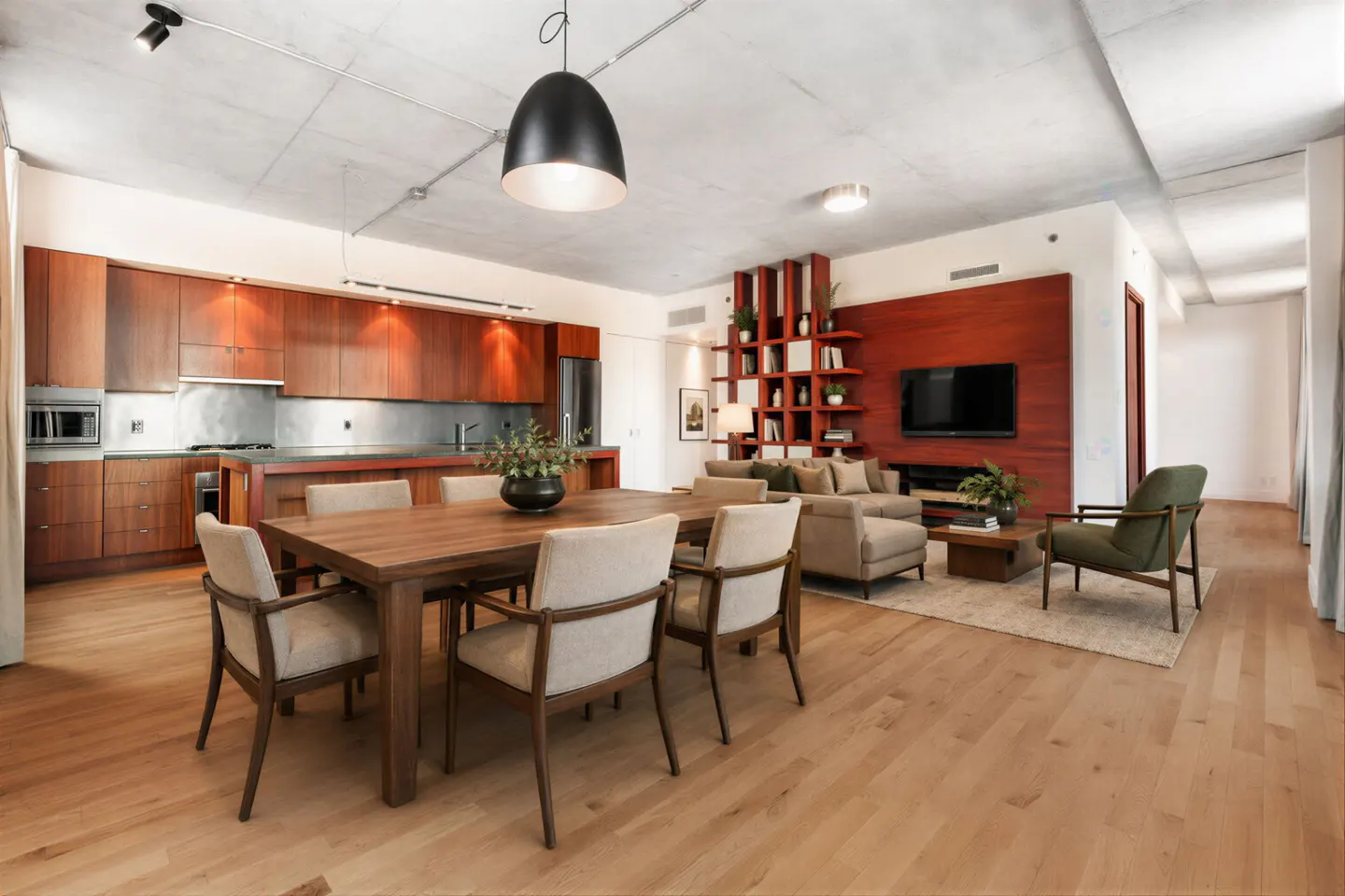 Open-concept living space with wood floors, a dining table, and a kitchen with wood cabinets. A living room with a TV and sofa is in the background.