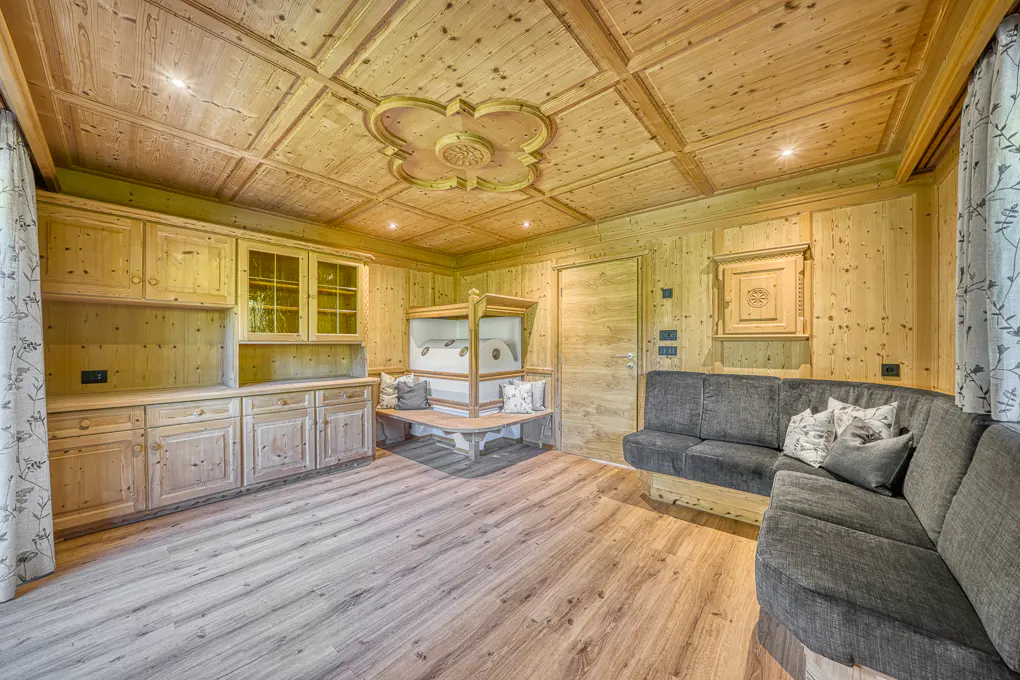 Living room with wood paneled walls, ceiling, and floor. A gray sectional sofa sits near a built-in cabinet and a Murphy bed.
