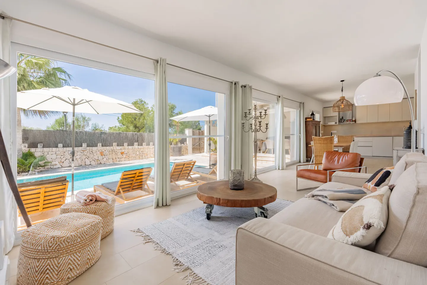 Bright living room with a beige sofa, brown leather chair, and a view of a pool through large windows.