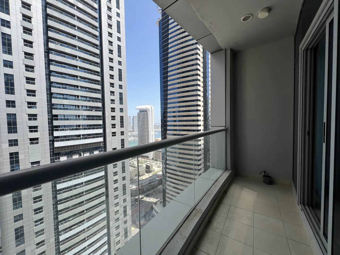 Balcony view of skyscrapers with glass railing and tiled floor. Gray walls and sliding glass door to the right.