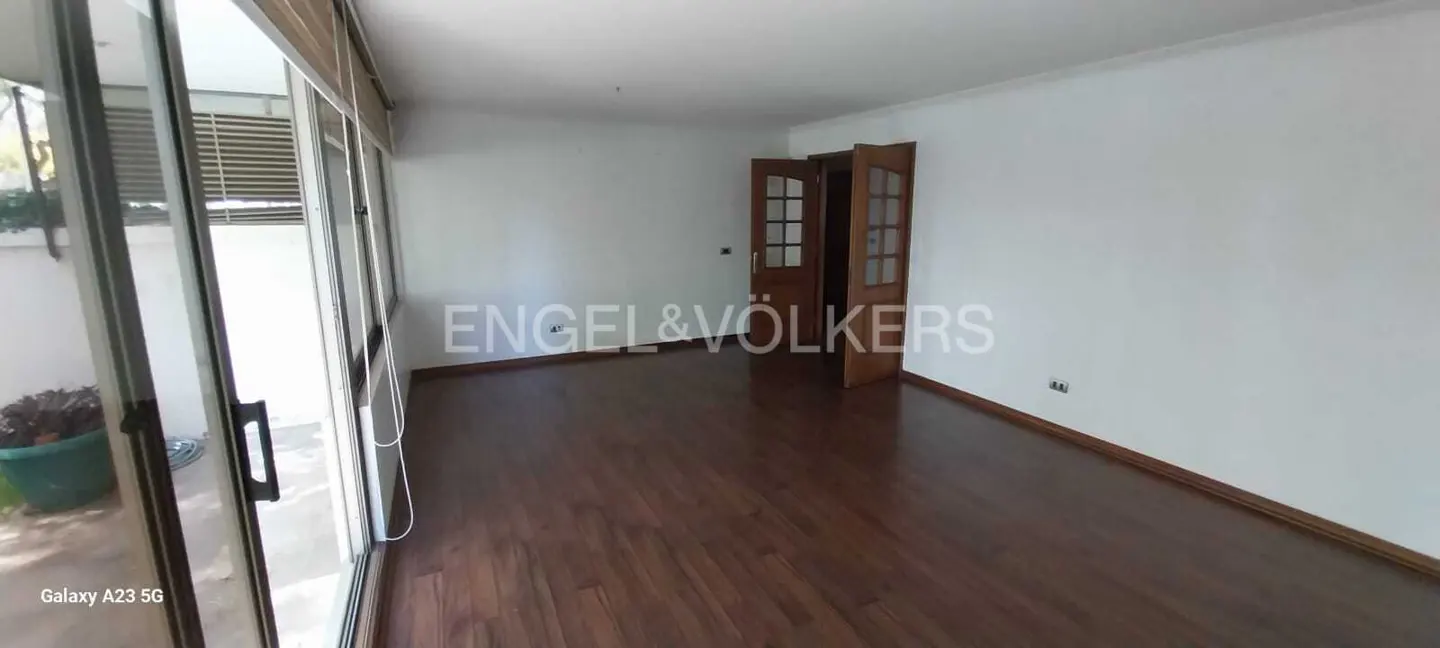 Empty room with dark wood floors, white walls, and glass doors to a patio. Wooden doors are open. Engel & Völkers logo is visible.