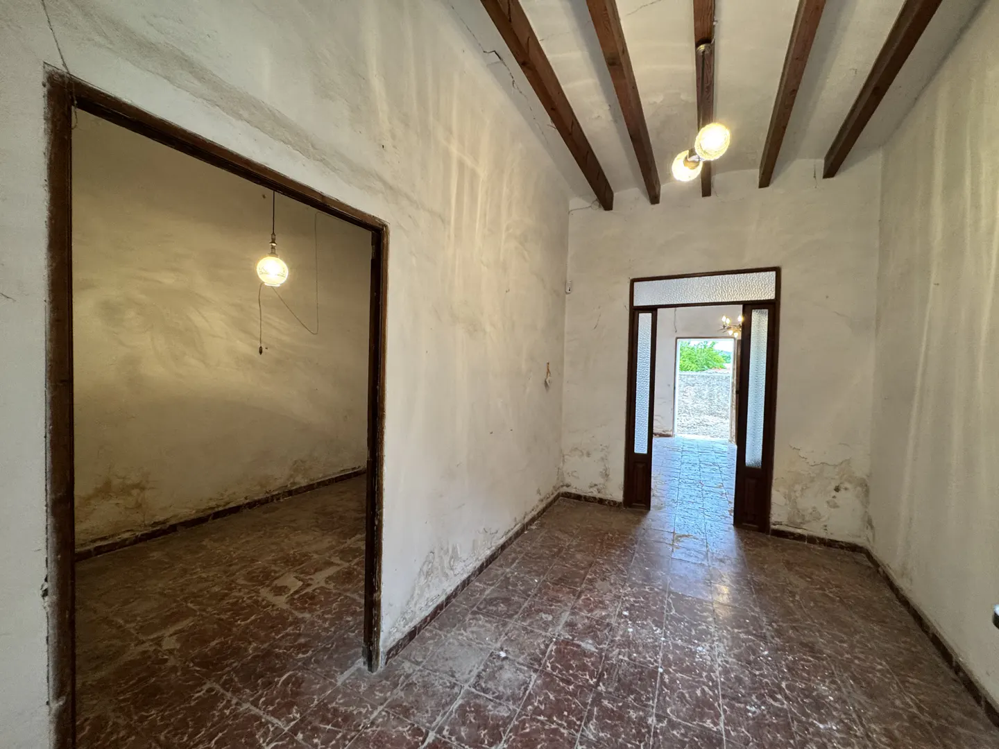 A room with white walls, a red tile floor, and wooden beams on the ceiling. Two doorways are visible.