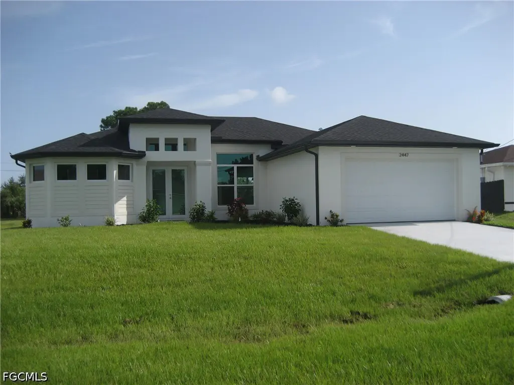 Modern white single-story home with a dark roof, two-car garage, and a large green lawn under a clear blue sky.