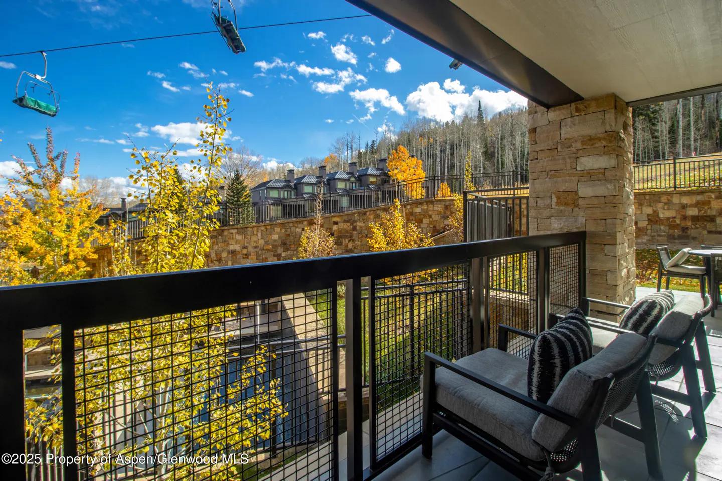 Balcony view of Aspen, Colorado, with chairs, fall foliage, ski lift, and blue sky.