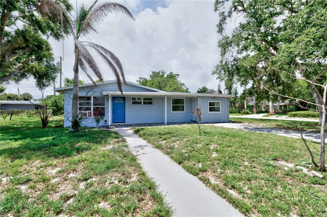 A light blue single-story house with a bright blue front door and a concrete walkway leading to it.
