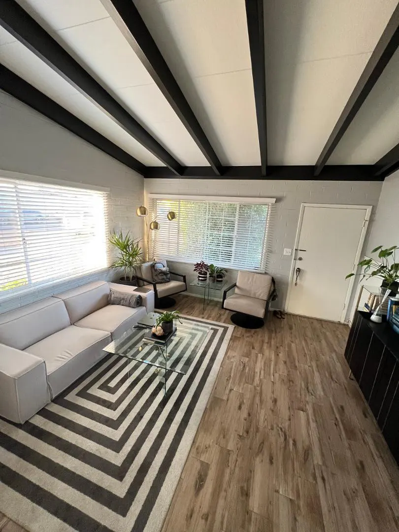 Living room with a gray sectional sofa, glass coffee table, and black and white chevron rug. Two chairs face a window with blinds.
