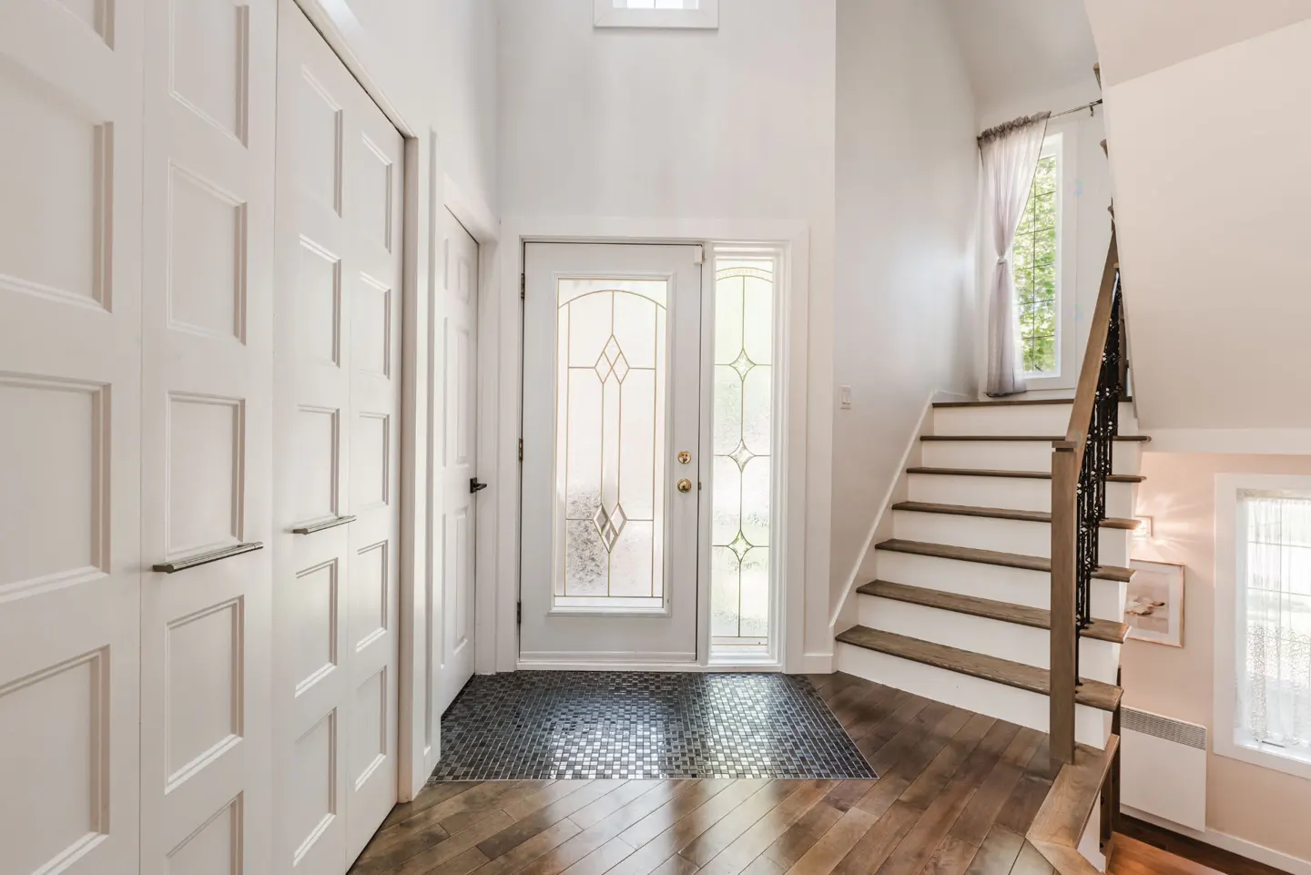 Bright entryway with white walls, a glass-paneled front door, dark wood floors, and a staircase with a decorative railing.