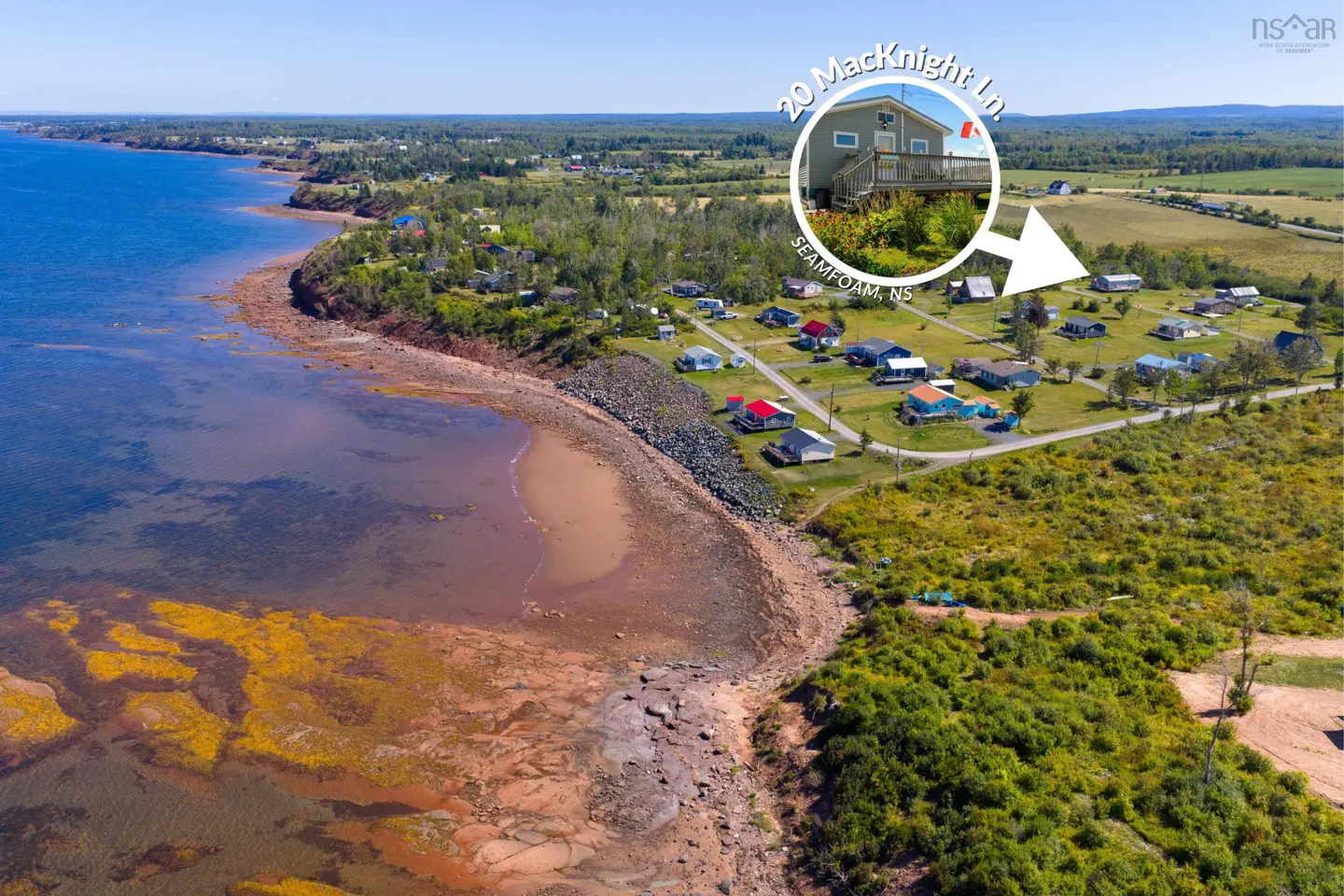 Aerial view of 20 MacKnight Ln, Seamfoam, NS, a gray house with a deck, near the ocean and other houses.