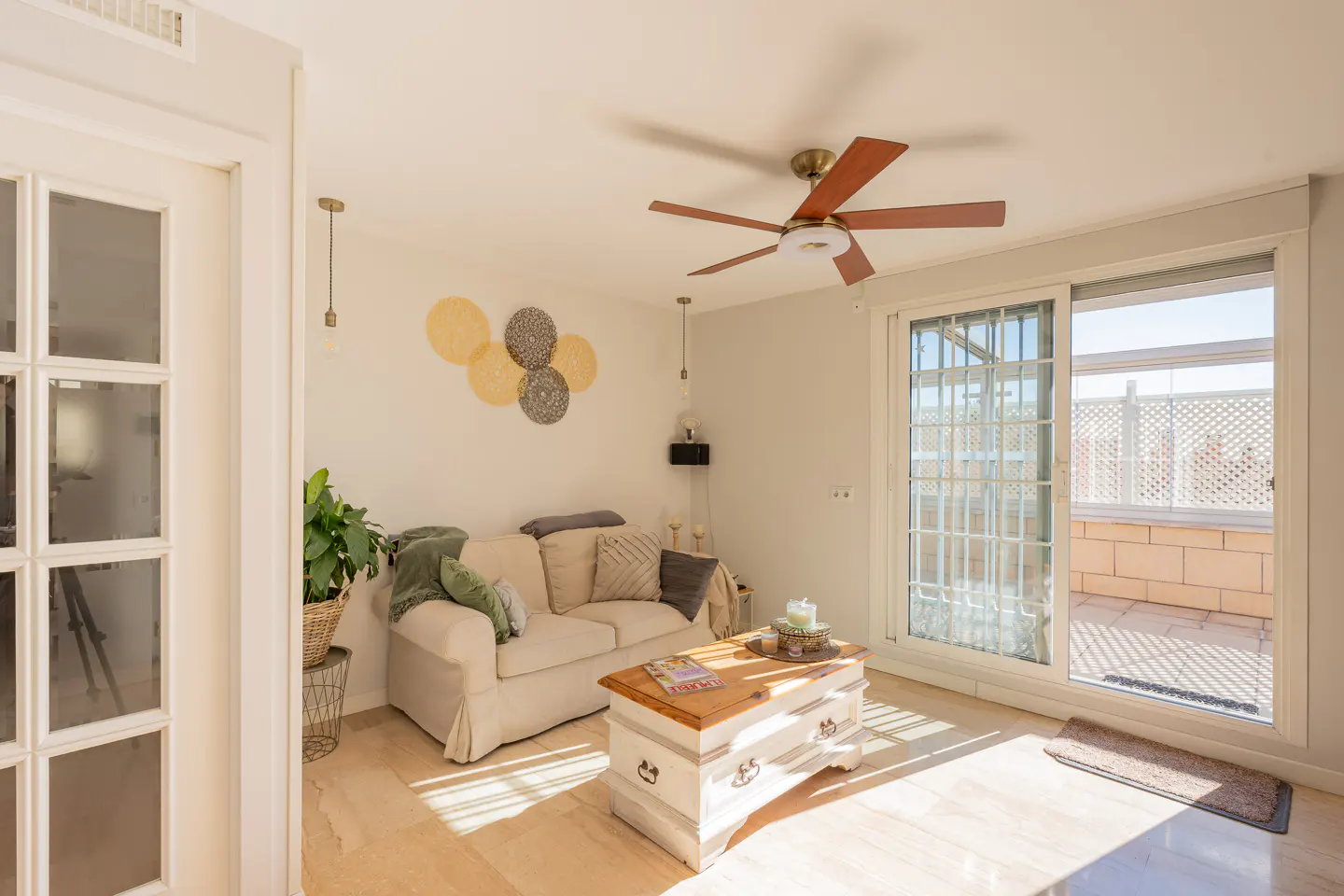 Bright living room with a beige sofa, wooden coffee table, and a ceiling fan. Sliding glass doors lead to a sunny patio.