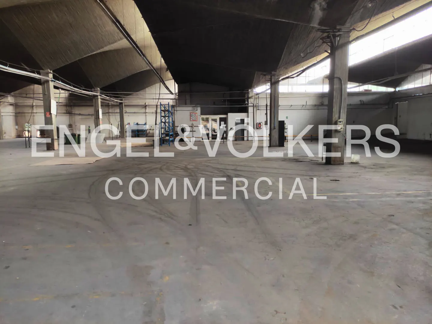 Large, empty industrial warehouse with concrete floors, high vaulted ceilings, and support pillars.