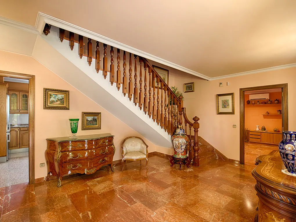 Elegant foyer with marble floors, peach walls, and a wooden staircase. Antique furniture and framed art add to the classic style.