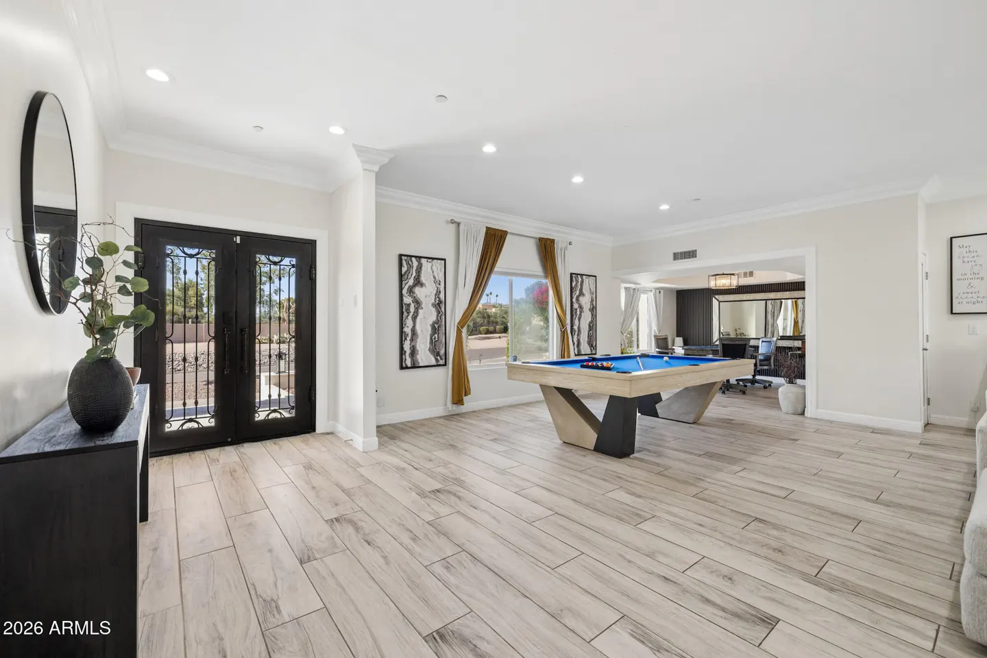 Spacious room with light wood-look tile floors, a blue pool table, and black double entry doors with decorative ironwork.